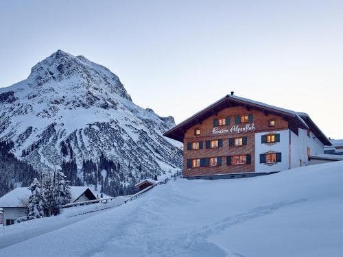 a building in the snow with a mountain in the background at Pension Alpenfluh in Lech am Arlberg
