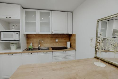 La cuisine est équipée de placards blancs, d'un lavabo et d'un miroir. dans l'établissement Apartman SLAVONIA ĐAKOVO, à Ðakovo