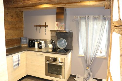 Il comprend une petite cuisine avec une cuisinière et une fenêtre. dans l'établissement La Maison des Charpentiers, à Zimmerbach