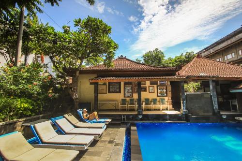 a woman sitting in lounge chairs next to a swimming pool at Legian Village Beach Resort - CHSE Certified in Legian