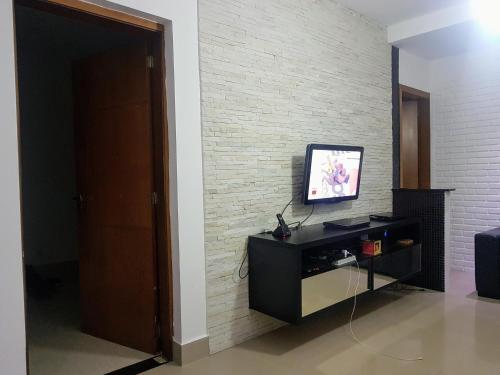 a living room with a tv on a brick wall at Quarto com Varanda - Recanto do Sabiá in Campinas