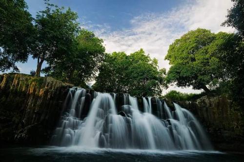 a waterfall in front of a rock wall with trees at Seaview Kite Studio - La Gaulette in La Gaulette