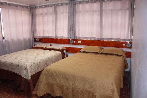 two beds in a room with windows and curtains at Kennedy Guest House in Cusco