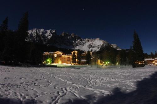 a lodge in the snow at night with snow covered mountains at Residence Grand Hotel Carezza in Nova Levante