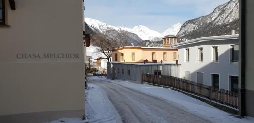 a snow covered street in a town with snow covered mountains at Chasa Melchior in Zernez
