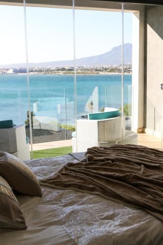 a bed in a bedroom with a view of the ocean at GORDON's SHORE LUXURY APARTMENTS - Solar Powered in Gordonʼs Bay