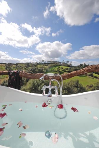 a hot tub with a view of the rolling hills at Freshwaterfarm Cottages - Muriwai in Waimauku