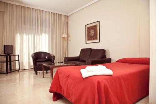 a hotel room with a red bed and two chairs at Apartamentos Olano C.B. in Madrid