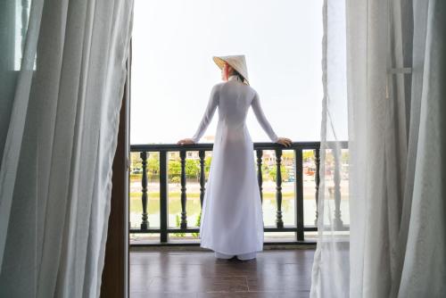 une femme en robe blanche debout sur un balcon dans l'établissement Little Hoi An . A Boutique Hotel & Spa, à Hội An