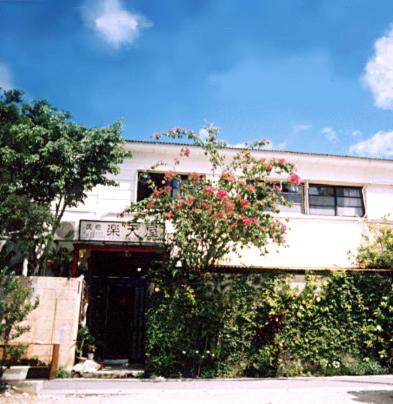 una casa blanca con una puerta y una planta con flores rojas en Minshuku Rakutenya, en Ishigaki Island