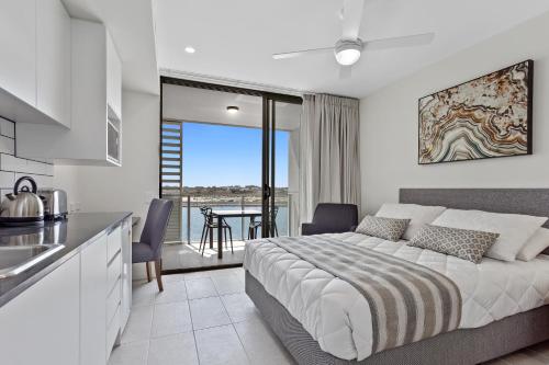 a bedroom with a bed and a kitchen with a balcony at North Shore Oceanside Kawana in Kawana Waters