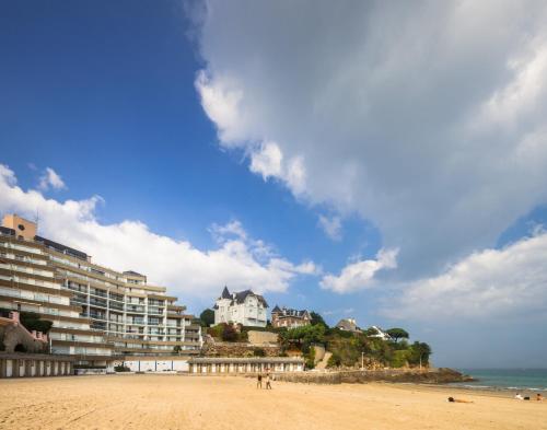 a beach with a building on a hill next to the ocean at Résidence Le Crystal Dinard Plage in Dinard