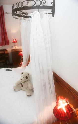 a teddy bear sitting on a bed next to a curtain at The Originals Boutique, Hôtel La Ferme du Pape, Eguisheim in Eguisheim