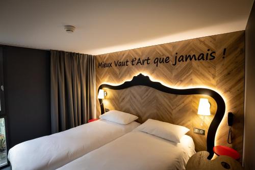 two beds in a hotel room with a sign on the wall at ibis Styles Douai Gare Gayant Expo in Douai
