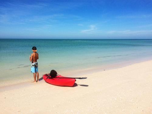 a man standing on a beach next to a red boat at Playa 55 beach escape - adults only Guesthouse in Celestún