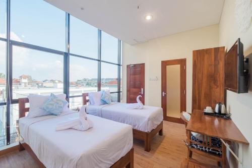 two beds in a room with large windows at Caroline Guest House in Canggu