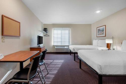 a hotel room with two beds and a desk and a table at Suburban Studios Huntsville University Area in Huntsville