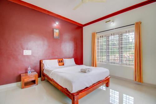 a bedroom with a red wall with a bed and a window at Holidayincoorg Orchid Villa in Madikeri