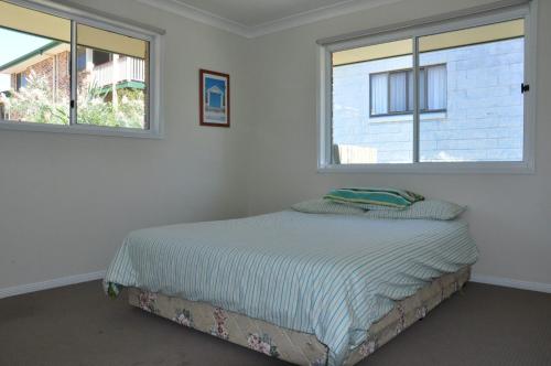 a bedroom with a bed with two windows at Rainbow Cottage in Rainbow Beach