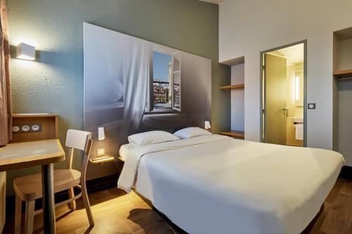 Un dormitorio con una gran cama blanca y una mesa en B&B HOTEL CAEN Sud, en Ifs