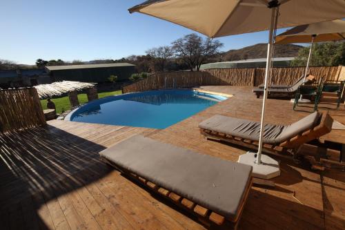 a swimming pool with two lounge chairs and an umbrella at Neuras Wine and Wildlife Estate in Naukluft Mountains