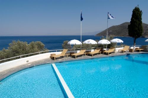 a swimming pool with chairs and umbrellas and the ocean at Kerveli Village Hotel in Kerveli