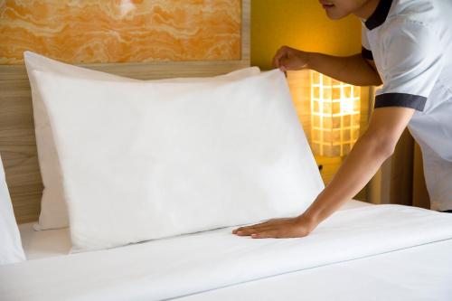 a man making a bed in a hotel room at Front One Akshaya Hotel Karawang in Karawang