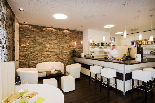 a restaurant with a bar with white chairs and a man behind the counter at Flair Hotel zum Schiff in Meersburg