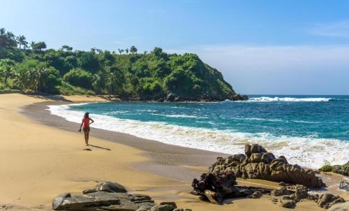 a woman walking on a beach next to the ocean at Casa Daikiri in Puerto Escondido