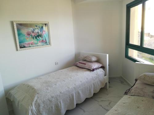 a white bedroom with a bed and a window at Apartment By The Lake in Tiberias