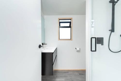 a white bathroom with a sink and a window at Cozy Tiny House Hideaway in Tauranga