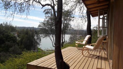 a wooden deck with two chairs and a view of a lake at Cabaña de Adobe en Lago Rapel in Lago Rapel