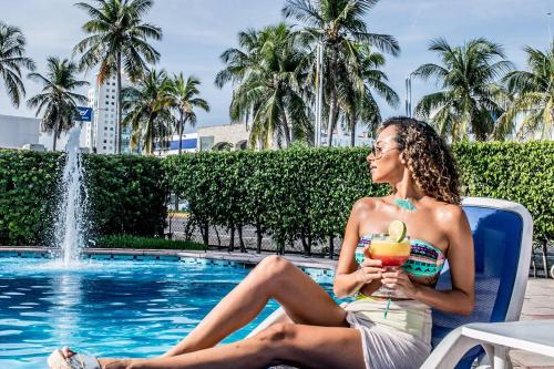 uma mulher sentada numa cadeira ao lado de uma piscina com uma bebida em Hotel Jaragua em Veracruz
