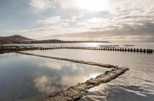 a body of water with a pier and the sun at Casa Playa Ondina in Gáldar