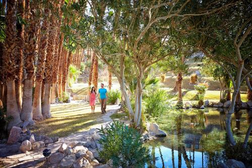 two people walking through a park with trees and a pond at The Inn at Death Valley in Death Valley