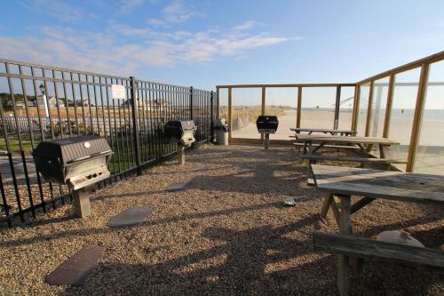 a fence with picnic tables and a grill next to the beach at Ocean Club on Smuggler's Beach in South Yarmouth