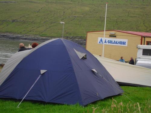 una tenda blu seduta sull'erba accanto a una barca di Giljanes Camping a Sandavágur
