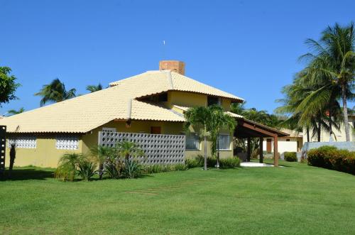 a yellow house with palm trees in a yard at LINDA CASA 4 QUARTOS CONDOMÍNIO PARQUE INTERLAGOS in Arembepe