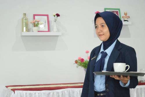 a woman in hijab holding a tray with a cup of coffee at Jambura Inn in Gorontalo