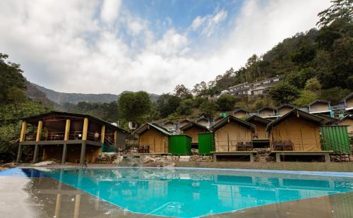 a row of wooden huts next to a swimming pool at Camp Bagheera in Rishīkesh