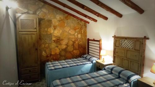 1 dormitorio con 2 camas y pared de piedra en Casas Rurales Cortijos el Encinar en Torres