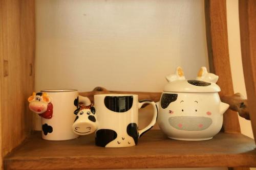 un estante con tres tazas de café y vacas. en Cow House, en Jian