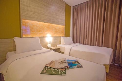two beds in a hotel room with a book on them at Front One Akshaya Hotel Karawang in Karawang