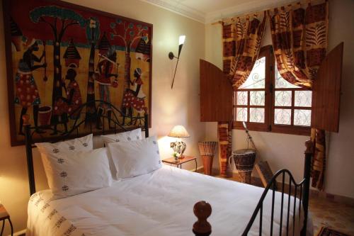 a bedroom with a white bed with a painting on the wall at Rive Du Lac in Lalla Takerkoust