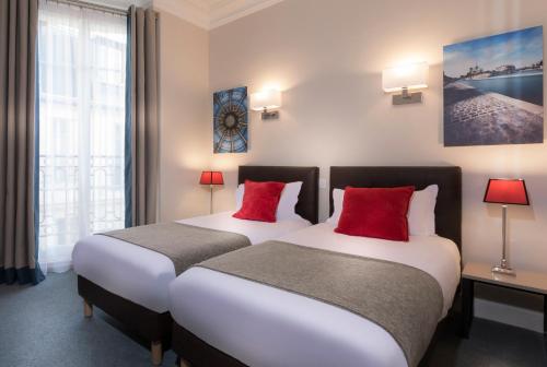 two beds in a hotel room with red pillows at Résidence Charles Floquet in Paris