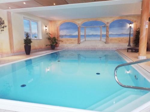 a large pool with blue water in a room with windows at Hotel Schaider in Ainring