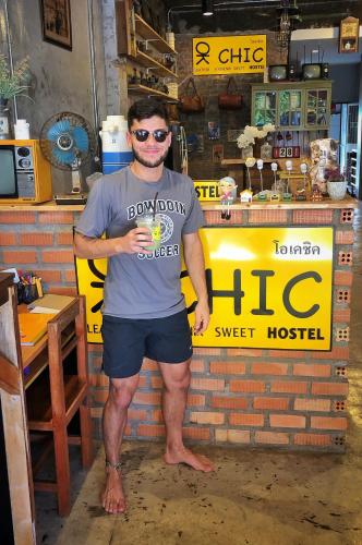 a man standing in front of a shop holding a drink at OK CHIC PHUKET HOSTEL in Phuket Town