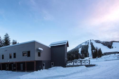 a building covered in snow with mountains in the background at Nowhere Special Hostel in Rossland