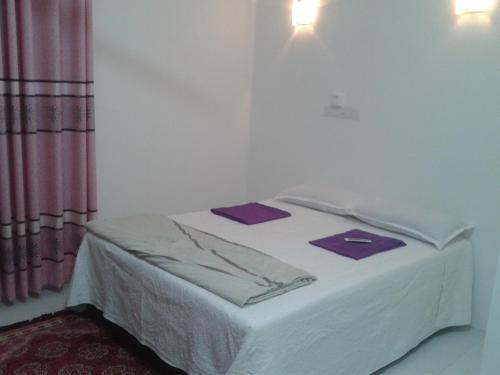 Una cama blanca en una habitación blanca con artículos morados. en Seri Kenangan en Kota Samarahan