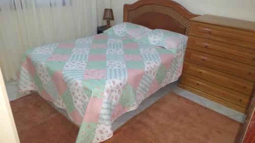 a bed with a pink and green quilt and a dresser at Casa para aluguel de verão in Torres